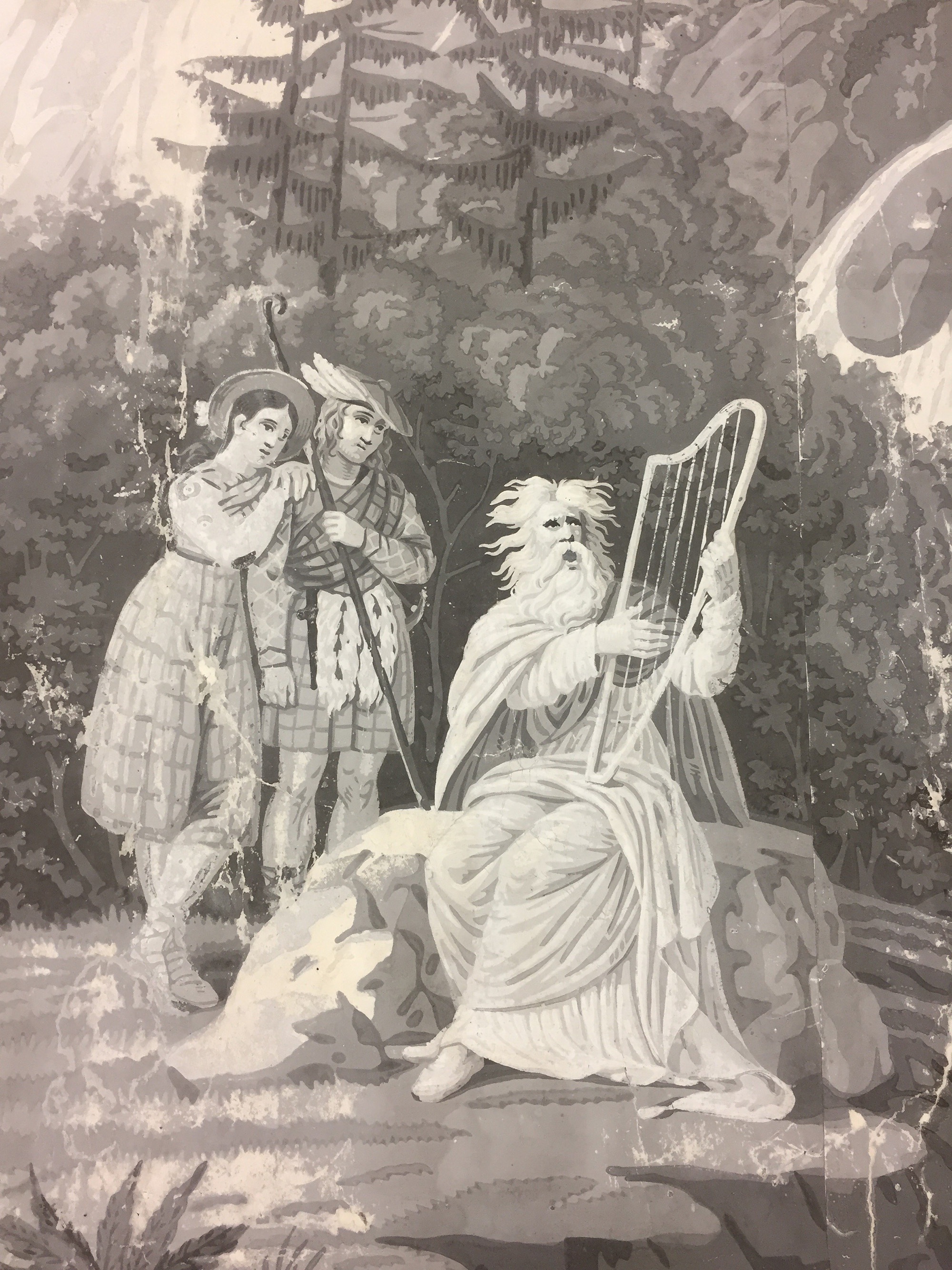 Valkopartainen mies soittaa harppua. Harpunsoittajan vieressä seisoo kaksi ihmistä, jotka ovat suunnanneet katseensa soittajaan. Taustalla metsää.